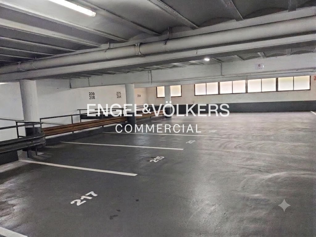Empty indoor parking garage with numbered spaces, white painted lines, and windows along the back wall.