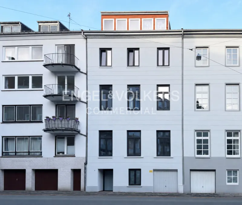 Exterior shot of a three-story white building with black framed windows and garage doors. Balconies are on the left building.