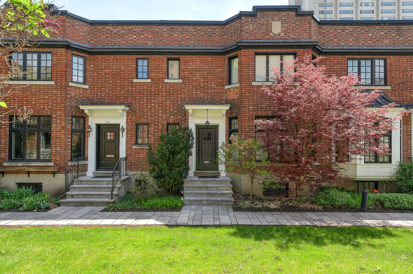 Row of red brick townhouses with black-framed windows, green doors, and manicured lawn.