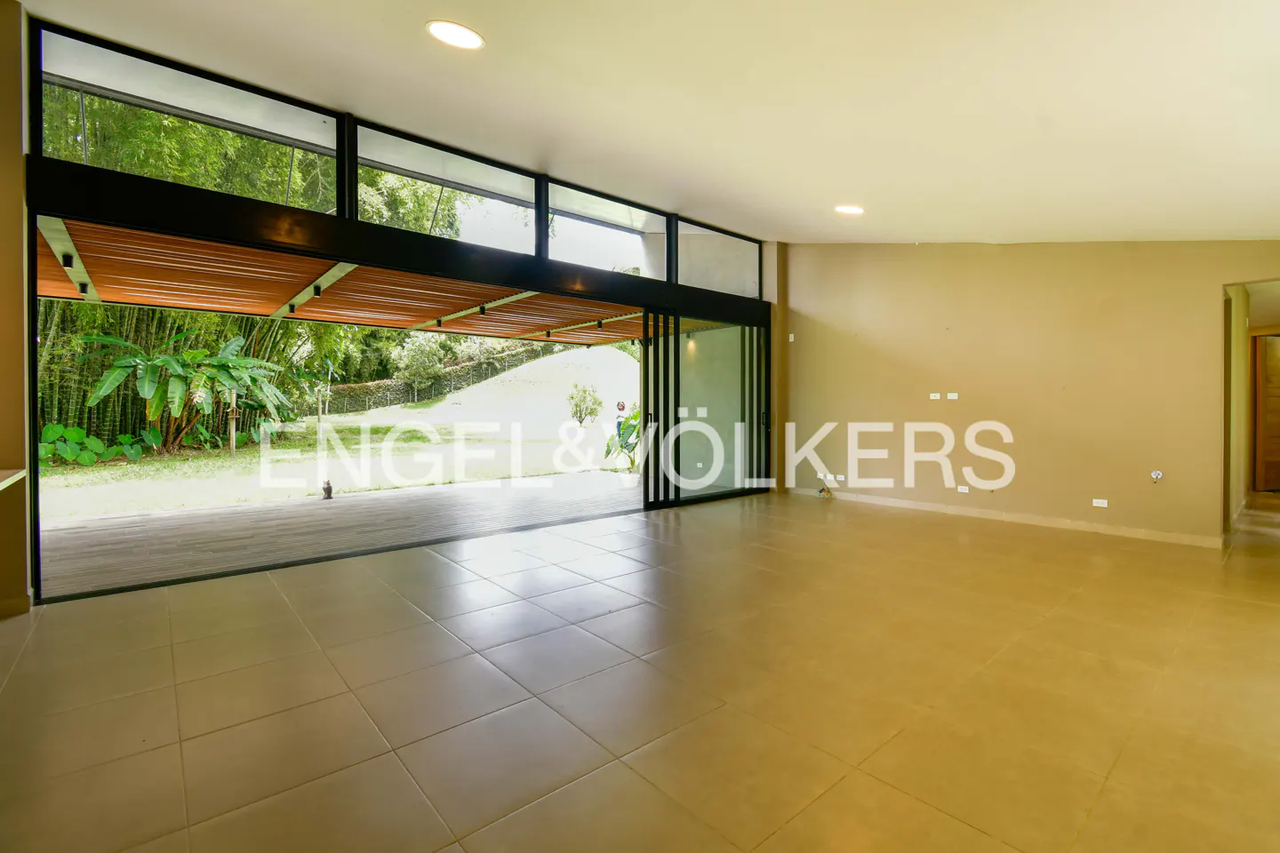 A bright, empty room with tan tile floors and a large sliding glass door to a green yard.