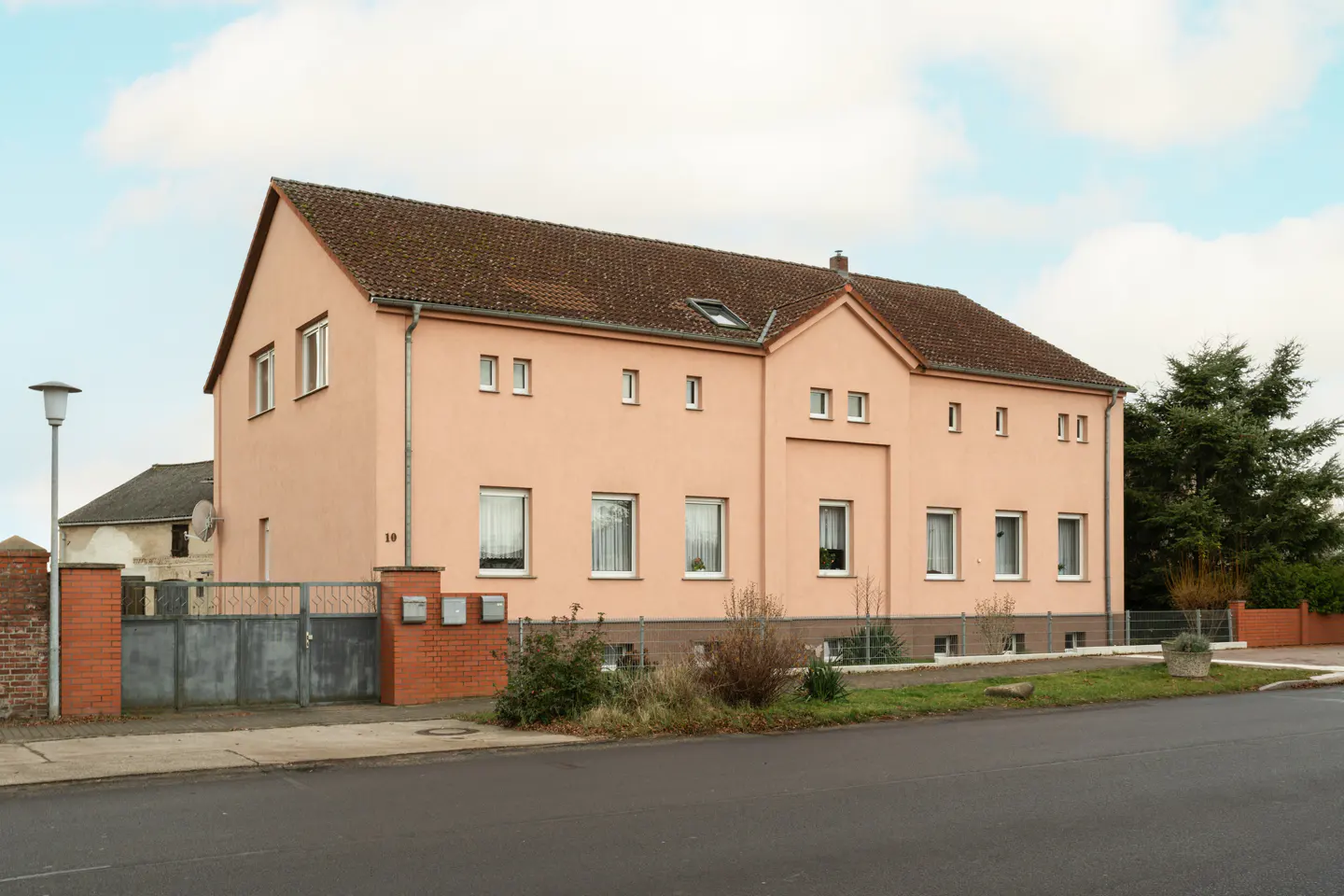 Two-story peach house with a brown roof, white-framed windows, and a gray metal gate. A street lamp stands to the left.