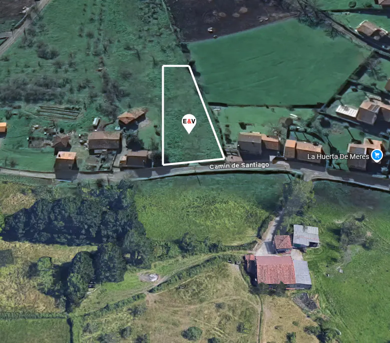 Aerial view of a green field outlined in white, marked "E&V," near "Camino de Santiago" road and rural buildings.