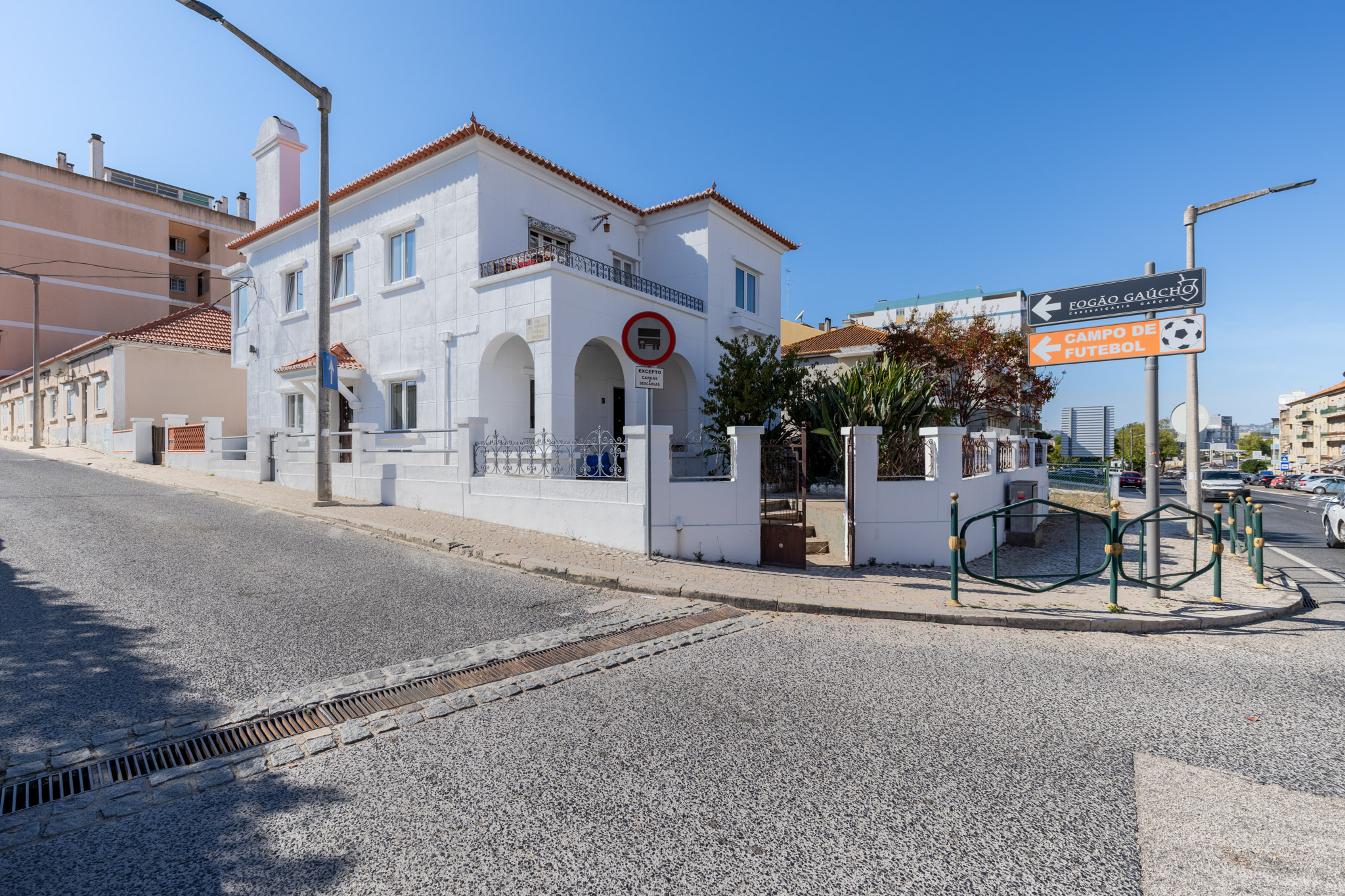 A two-story white house with arched entryways on a sunny street corner, featuring a no-entry sign and nearby road signs. [AI-generated text]