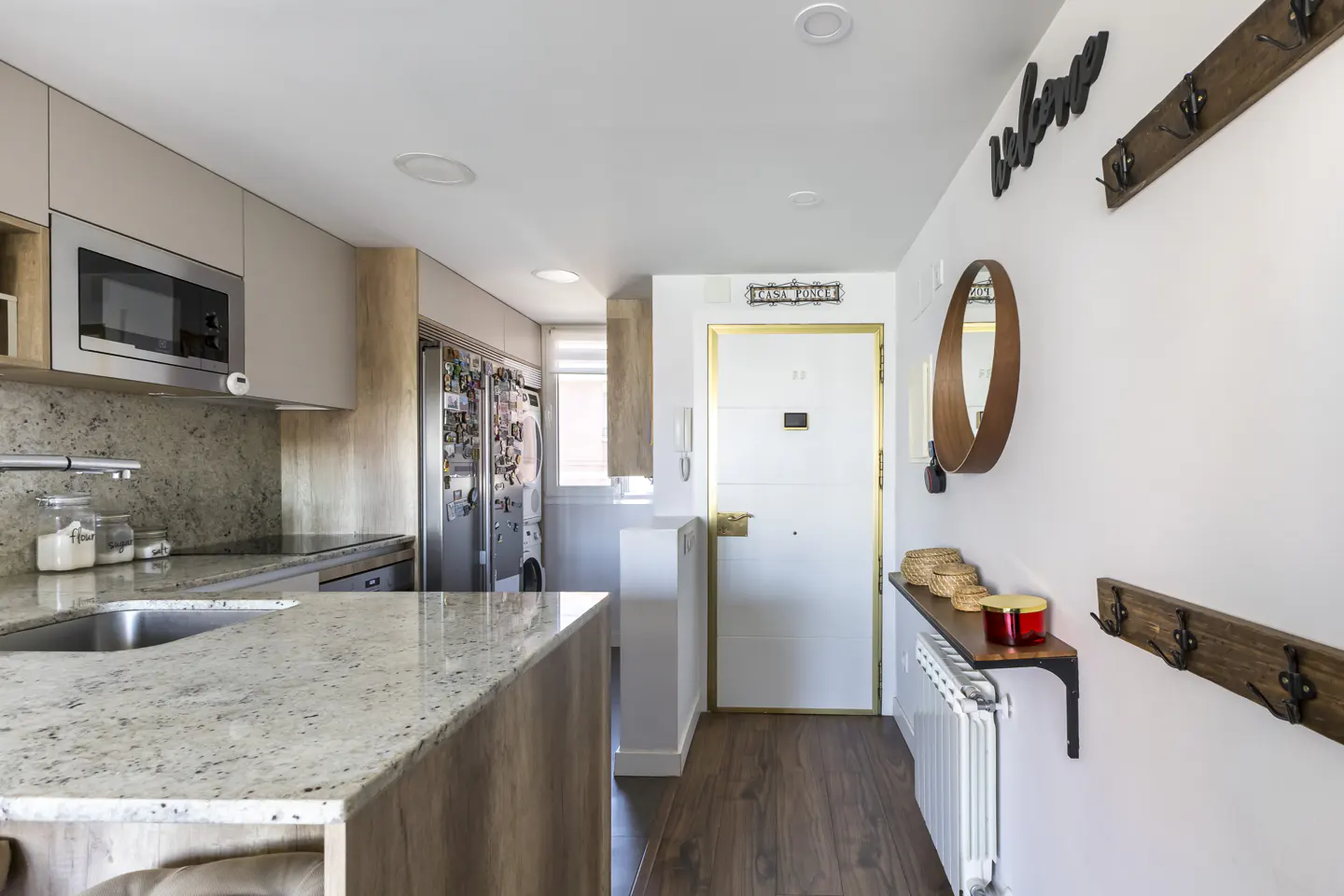 A bright, modern apartment interior with a kitchen island, white door, and hallway decor.