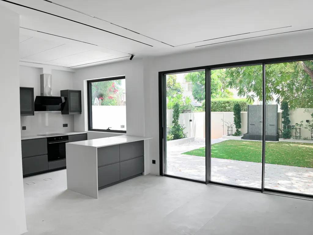 A modern kitchen with gray cabinets, white countertops, and large sliding glass doors to a green lawn.