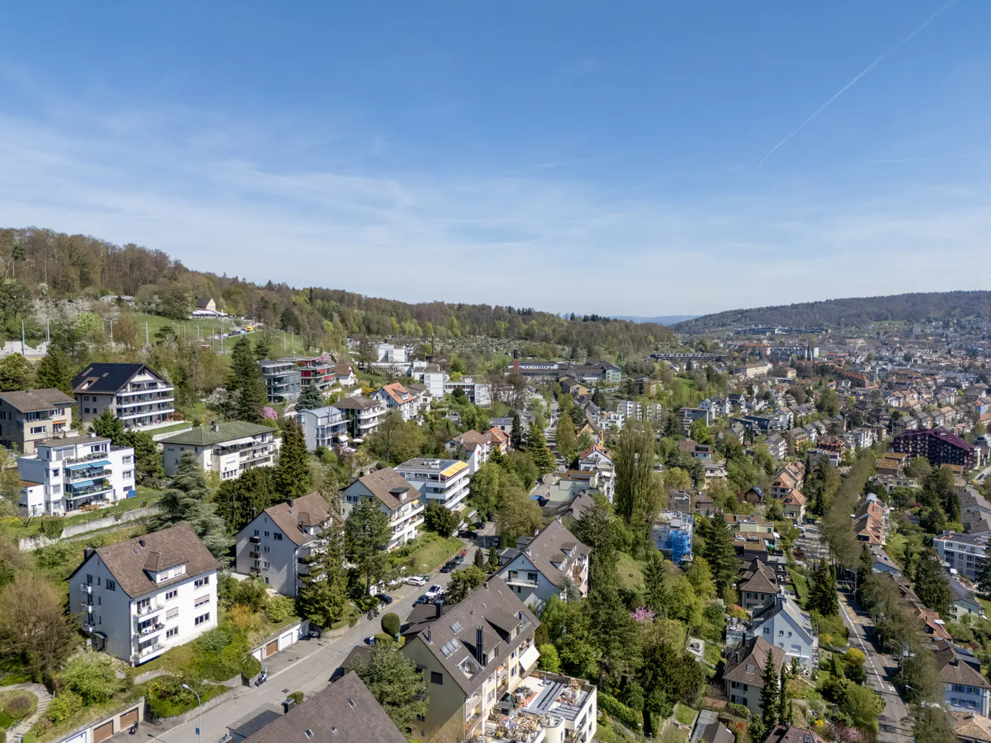 Aerial view of a hillside neighborhood with houses, trees, and a clear blue sky.