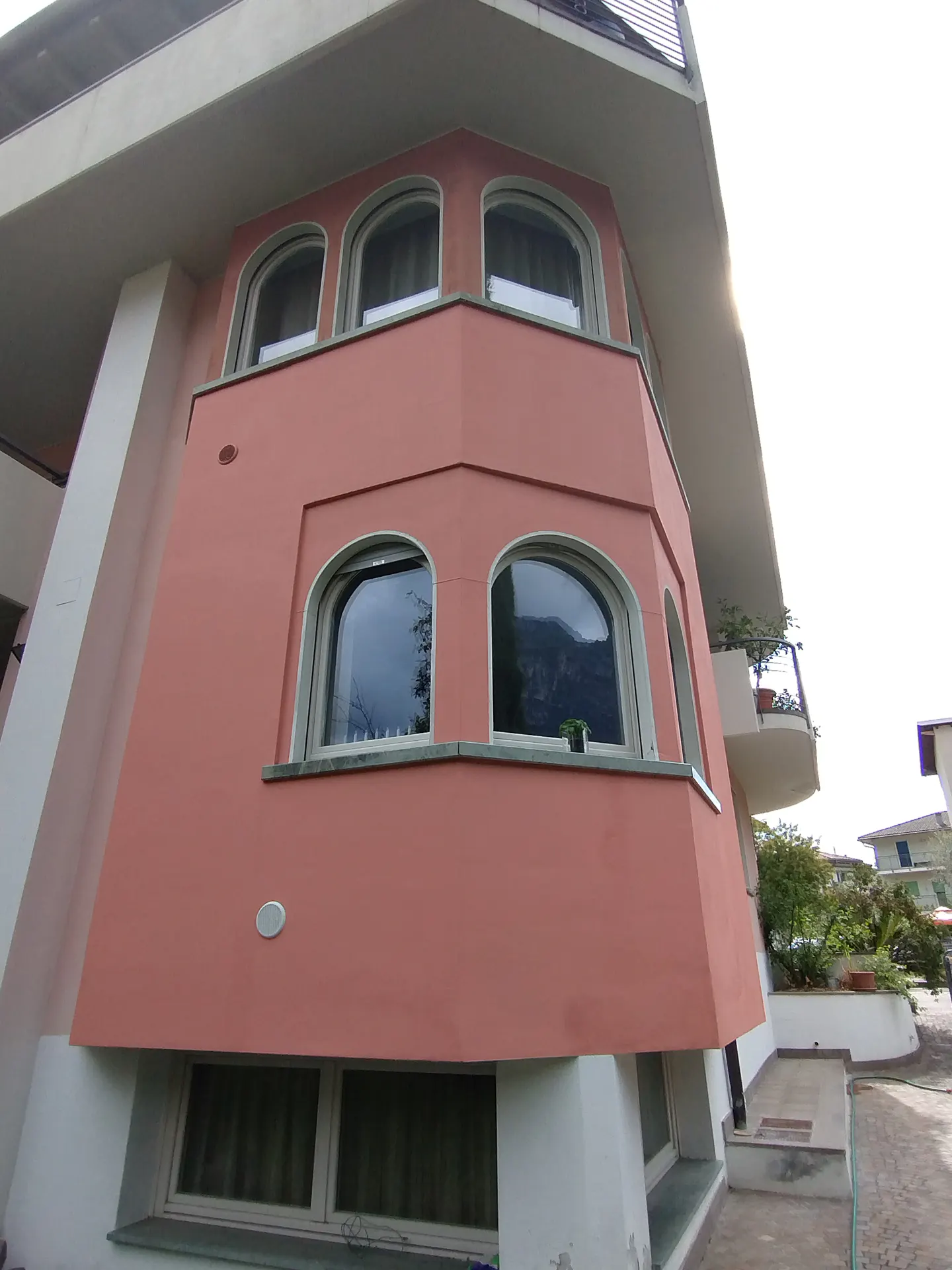 Low-angle view of a salmon-colored house exterior featuring arched windows and a white base, set against a bright sky.
