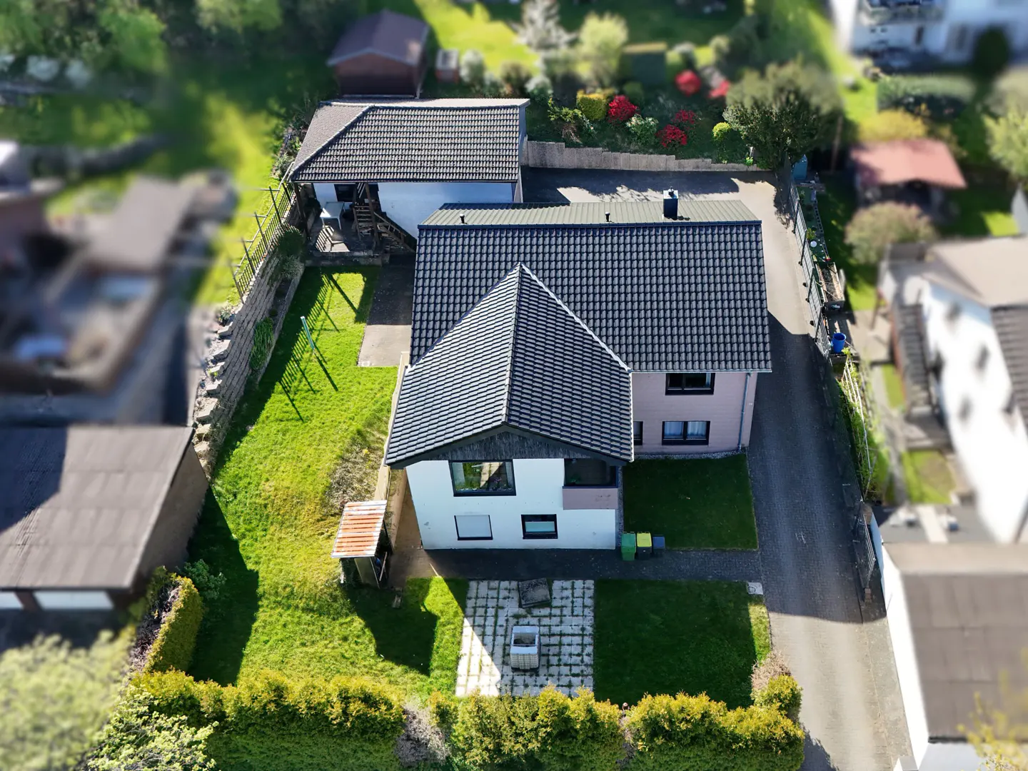 Aerial view of a two-story house with a dark gray roof, green lawn, and a stone patio in the backyard.