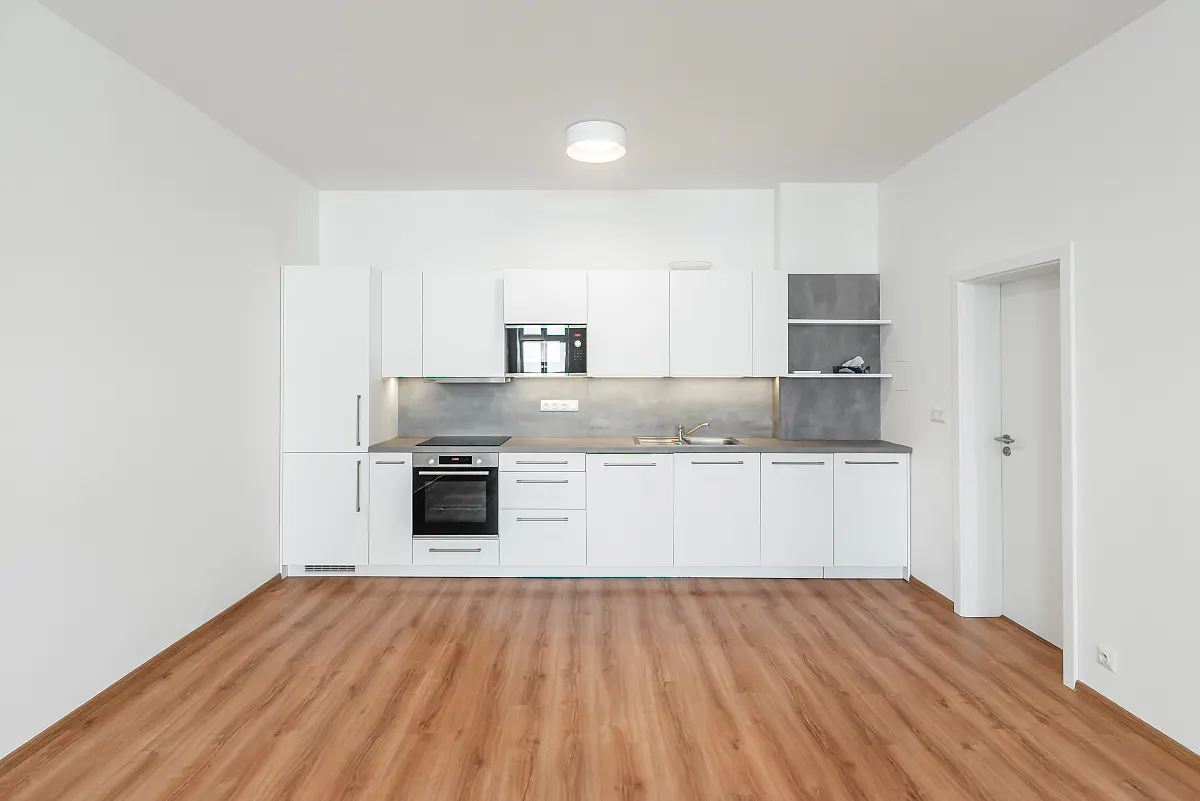 Bright, modern kitchen with white cabinets, gray countertops, and wood-look flooring. A door is visible on the right.