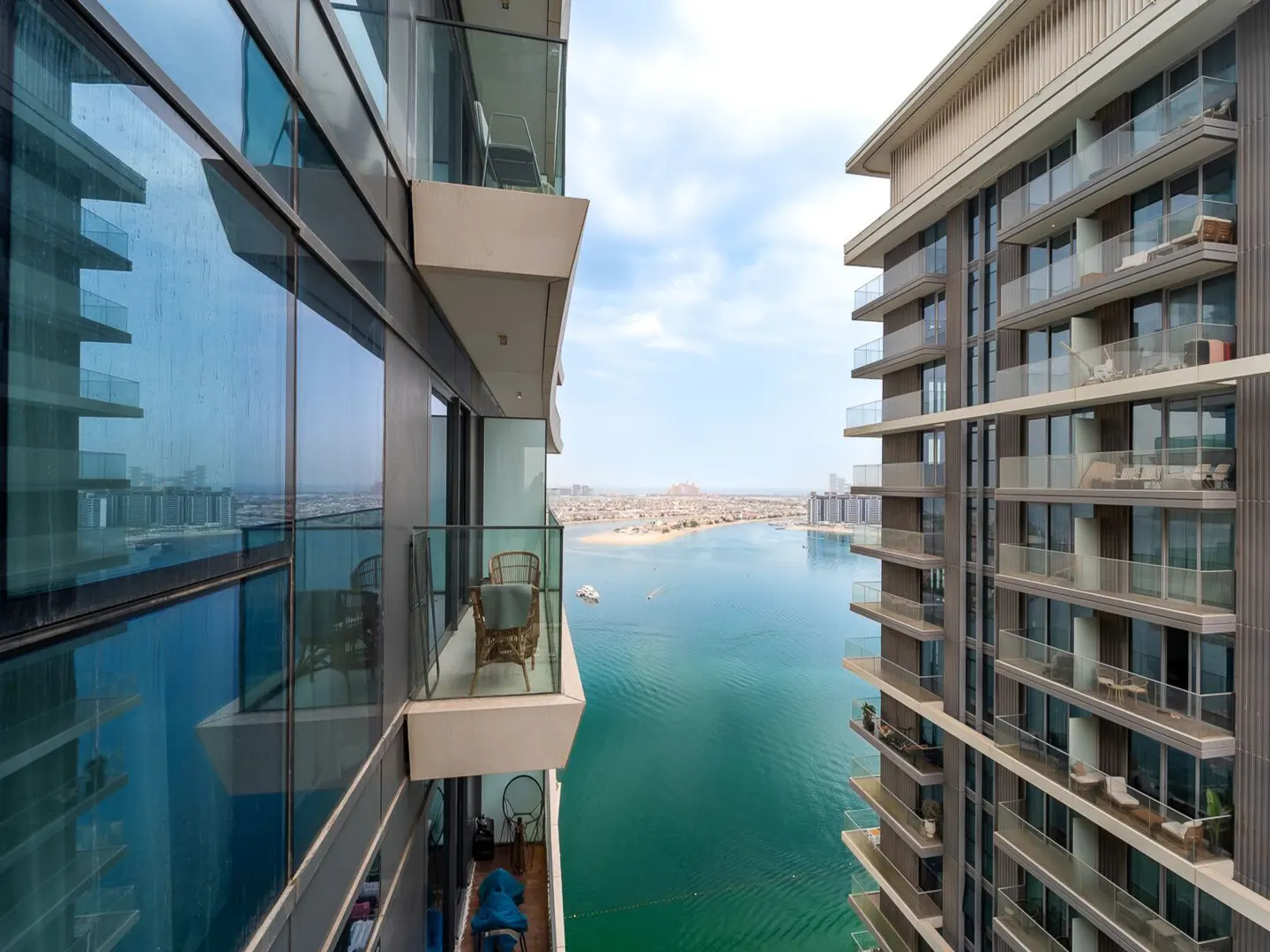 View between two modern high-rise buildings with glass balconies overlooking a turquoise bay and distant city skyline.