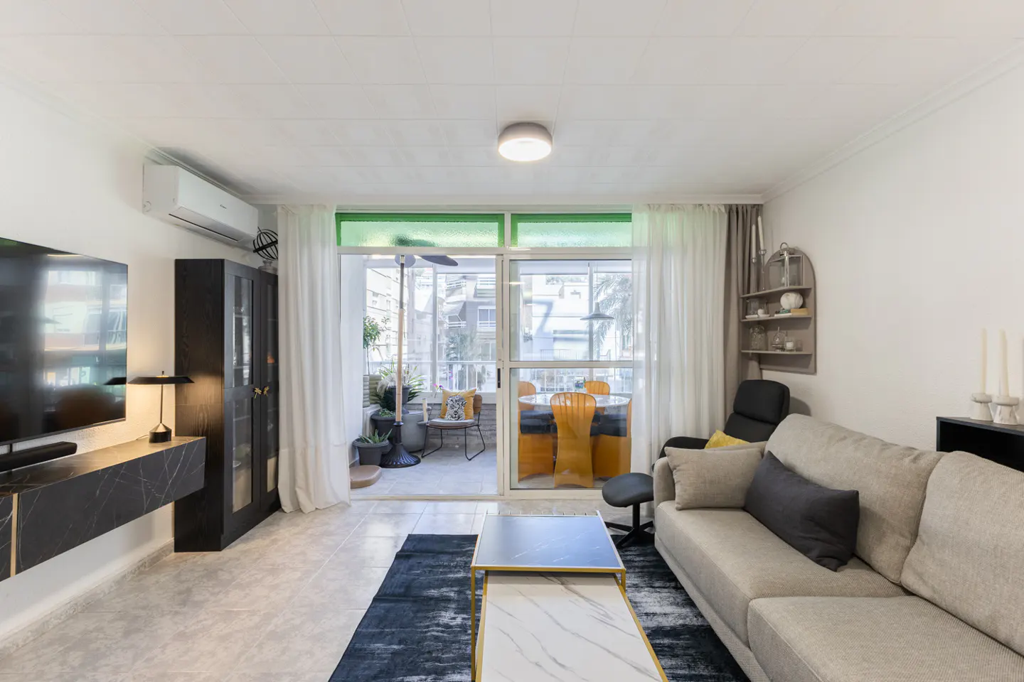 Bright living room with a beige sofa, black accent furniture, and a balcony with a table and chairs.