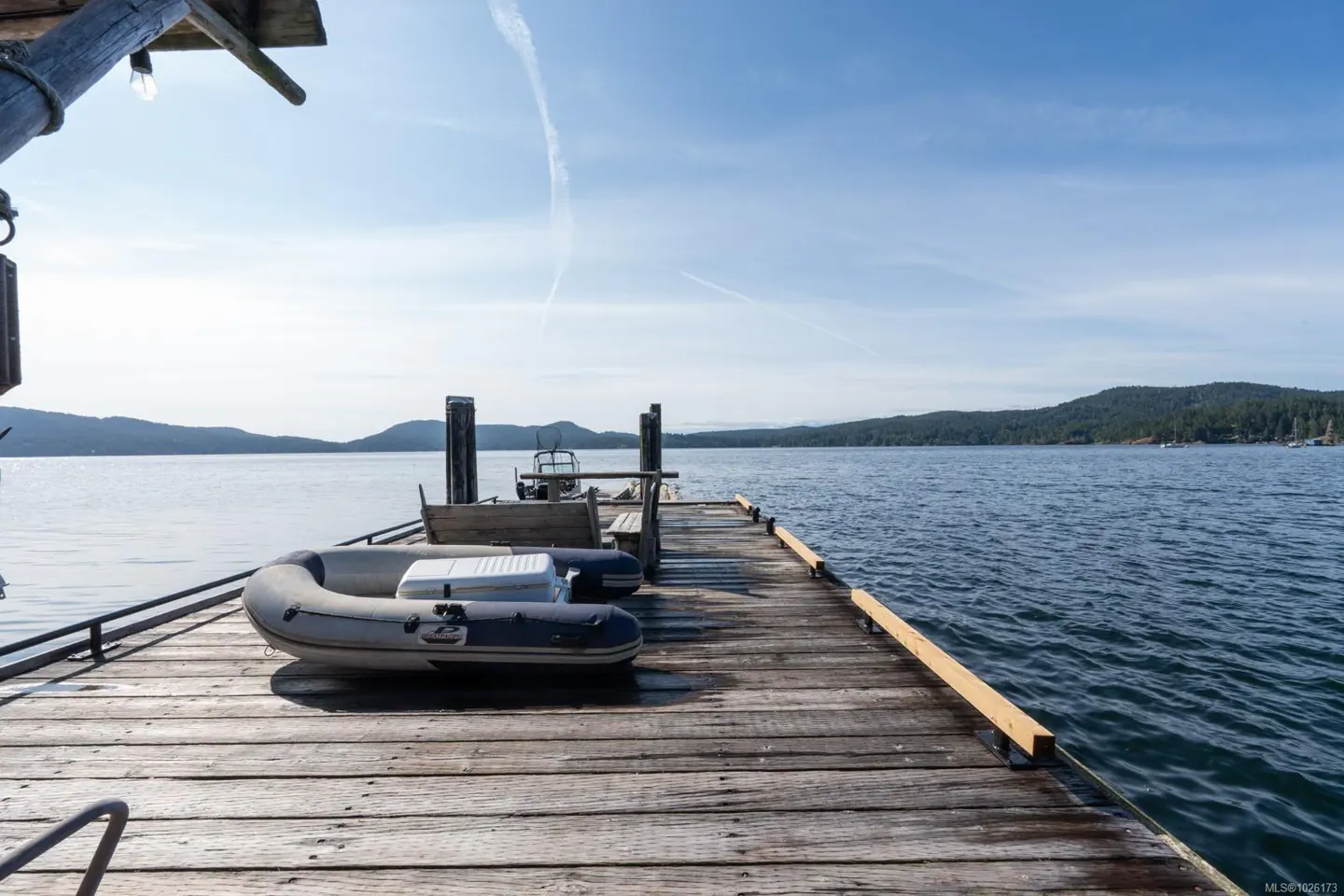 Wooden dock with an inflatable boat and small motorboat on a sunny day. Water and forested islands in the background.