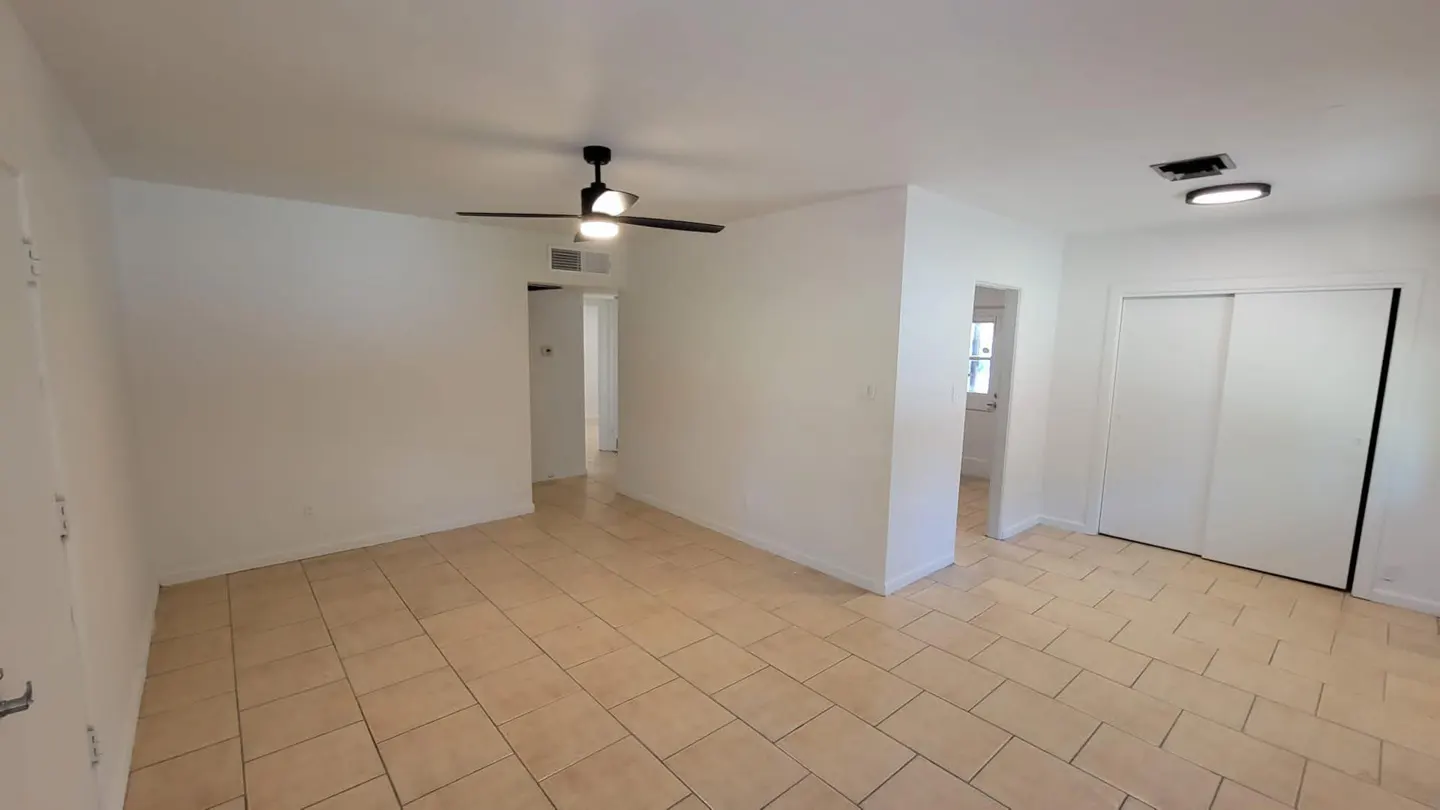 Empty room with beige tile flooring, white walls, and a black ceiling fan with lights. A closet with sliding doors is on the right.
