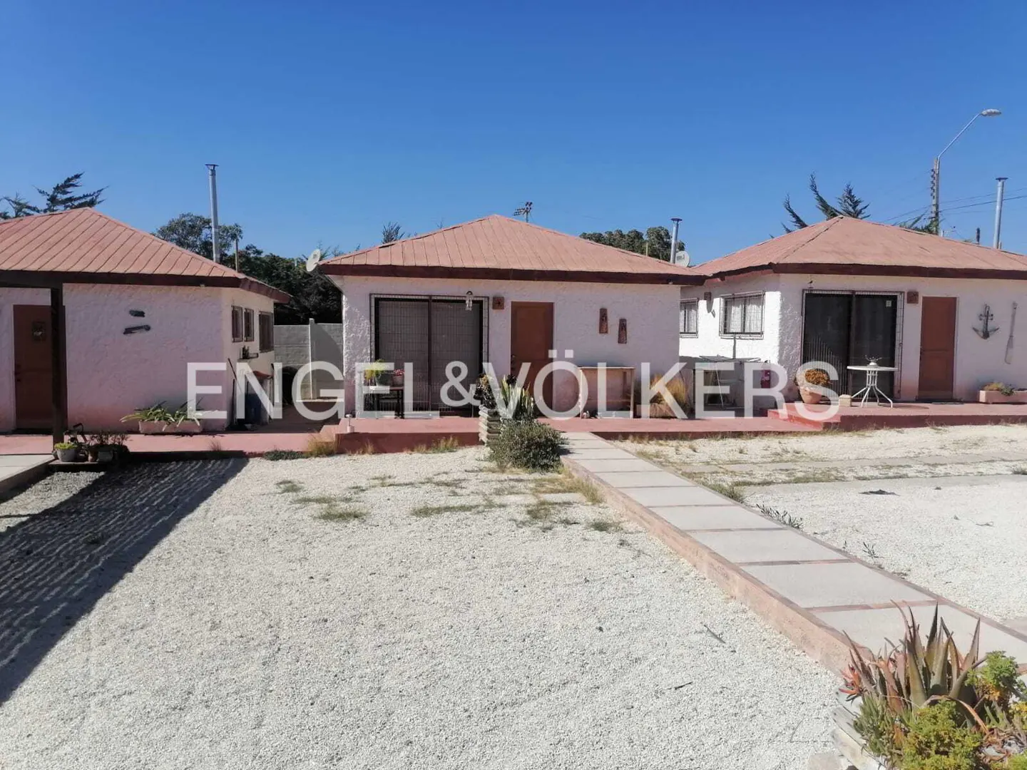 Three white single-story cottages with terracotta roofs and gravel yards under a clear blue sky.
