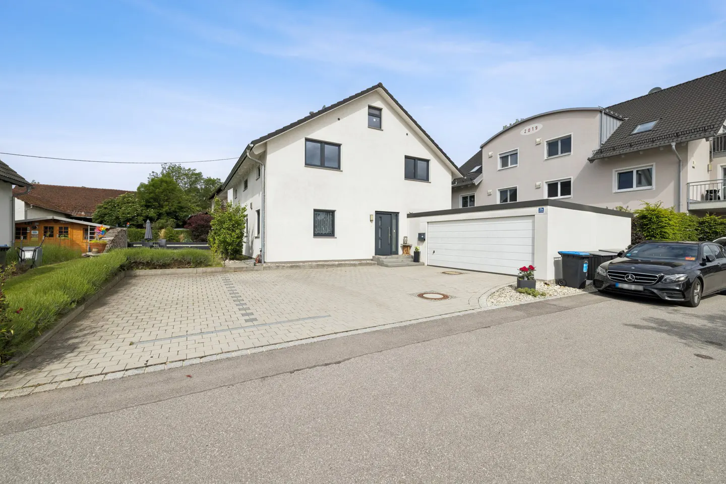 A two-story white house with a gray roof and black windows, a garage, and a paved driveway.