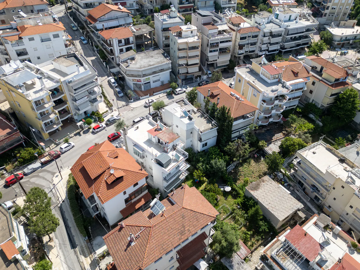 Aerial view of a dense residential neighborhood with multi-story buildings, terracotta roofs, and streets with parked cars.