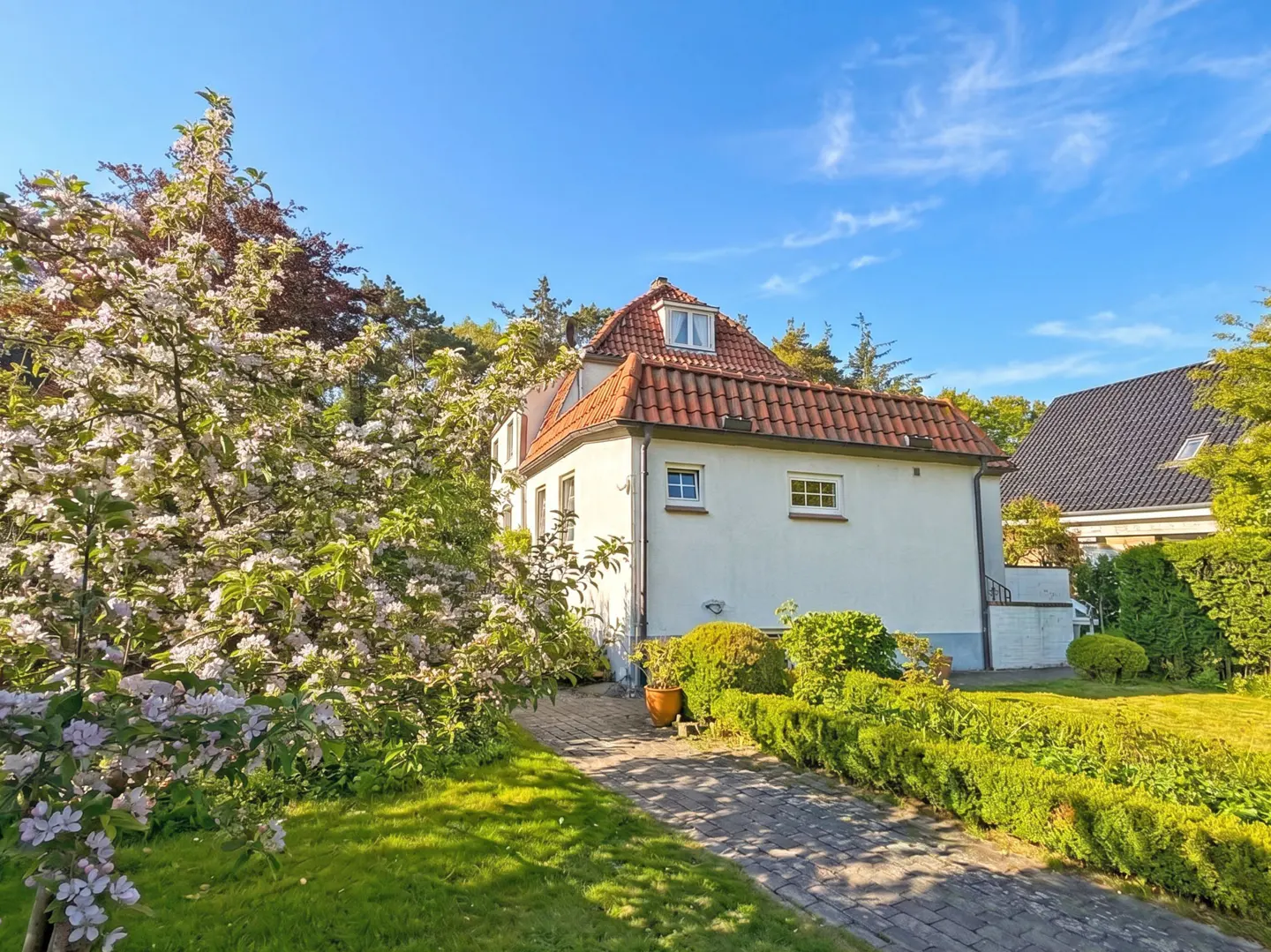Exterior of a white house with a red tile roof, blooming tree, and brick walkway.
