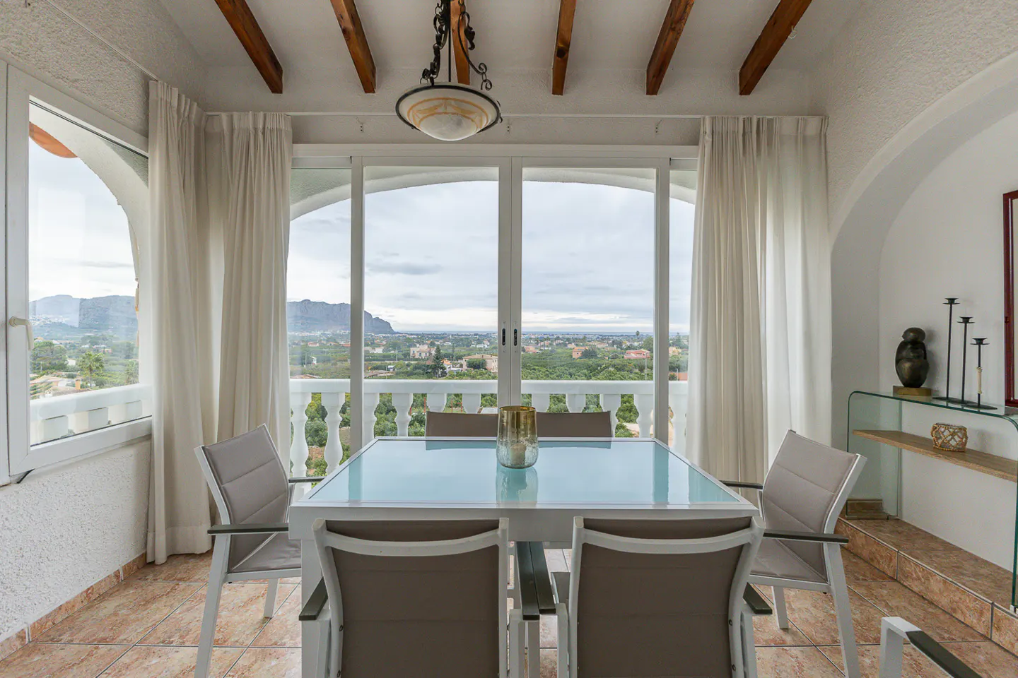 Indoor dining area with a white table, gray chairs, and a scenic view through a large window.