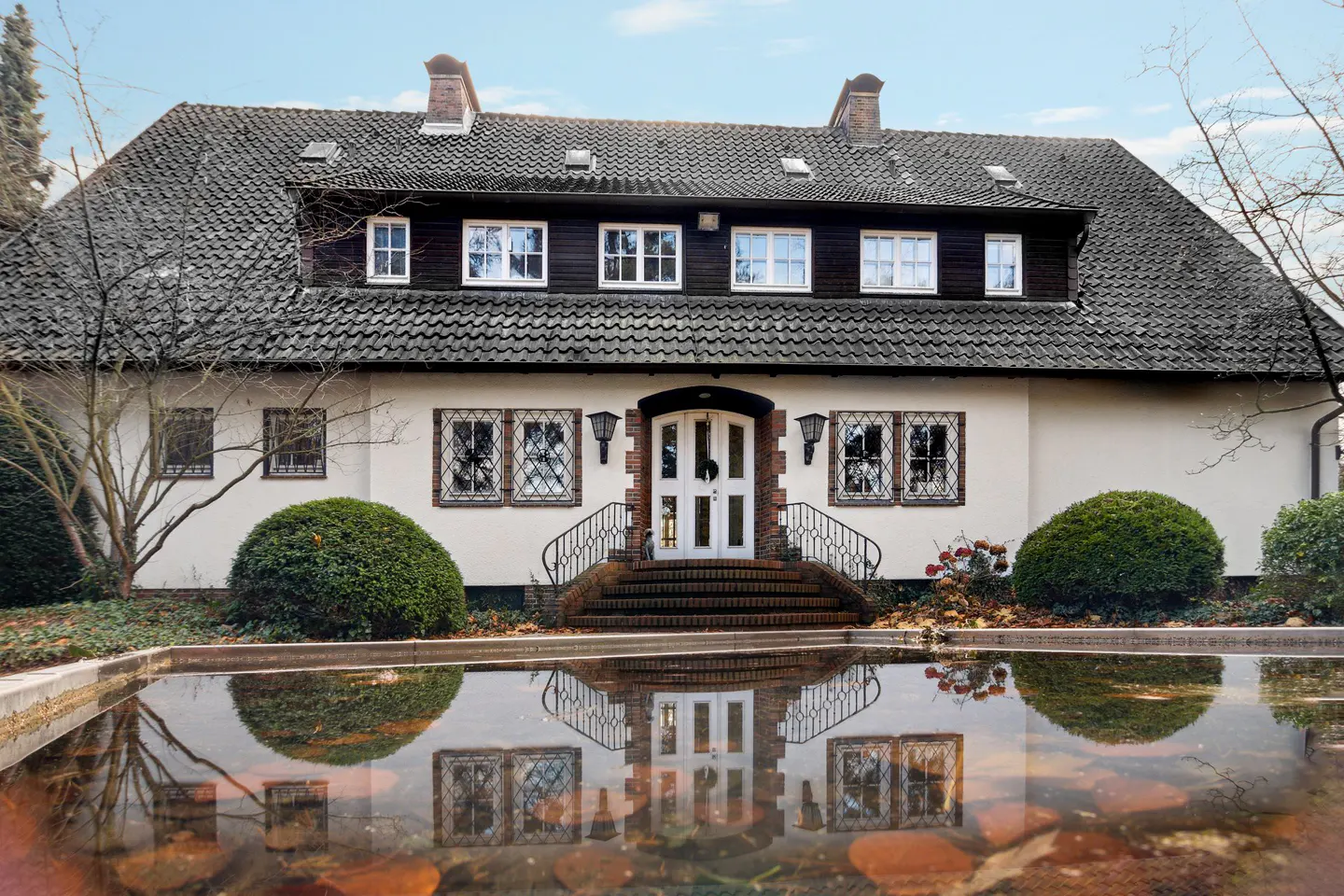 Two-story house with a gray roof, white walls, and a white front door with brick trim, reflected in a pool of water.