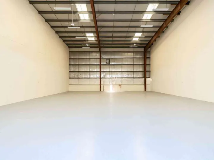 Empty warehouse interior with white walls, gray floor, metal beams, and a closed metal door at the back.