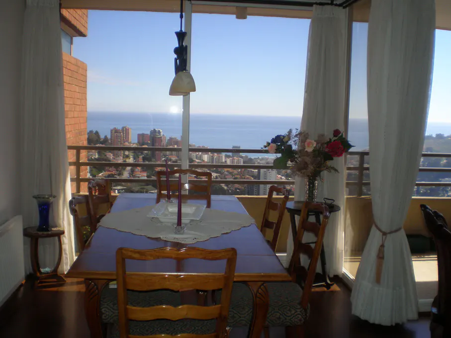 Dining room with a wood table and chairs, white curtains, and a city and ocean view.