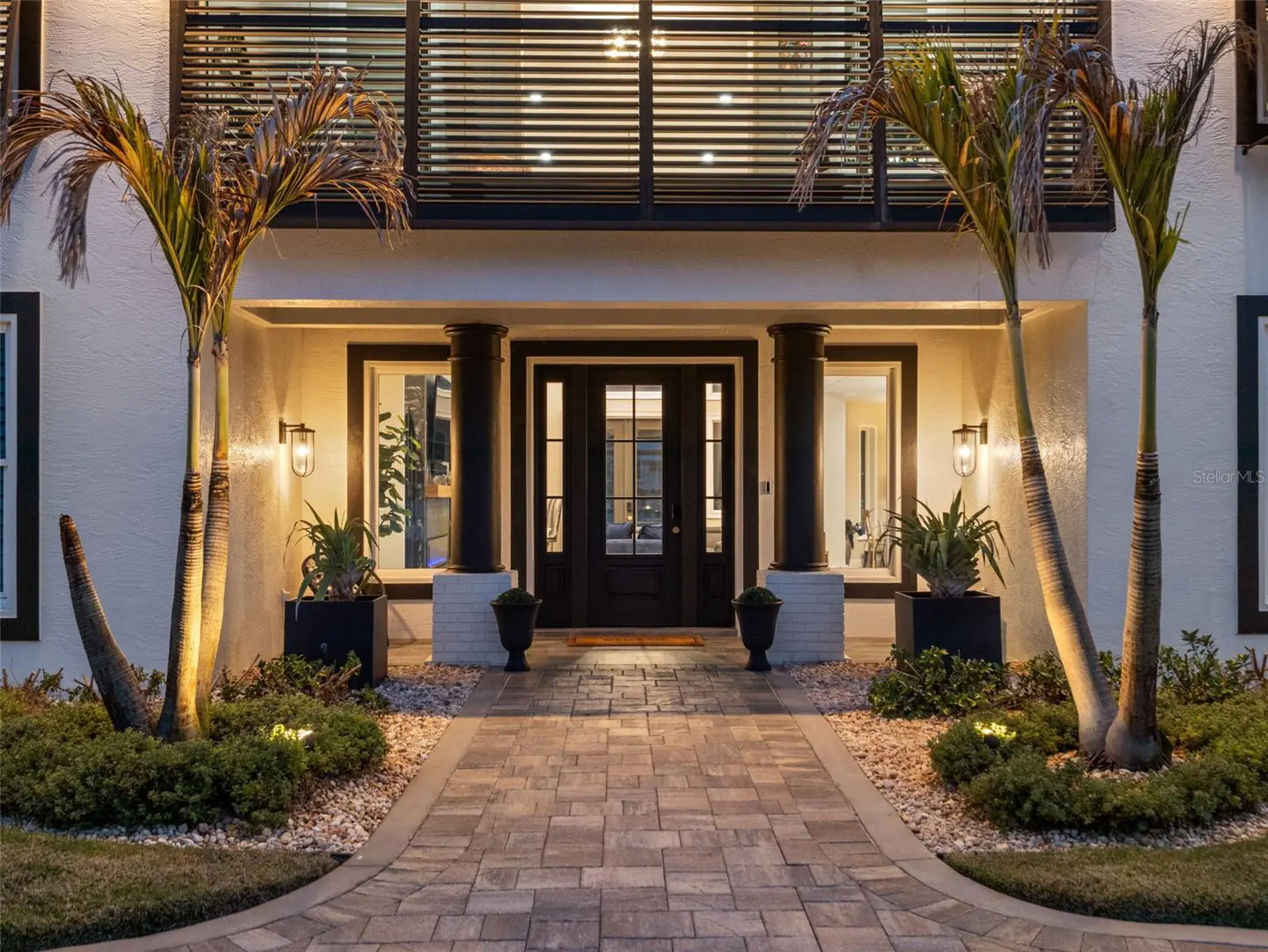 Exterior view of a two-story white house with black trim, a brick walkway, and two palm trees.