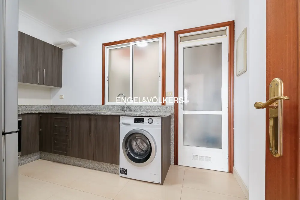 A kitchen with gray cabinets, granite countertops, a white washing machine, and a sliding window.