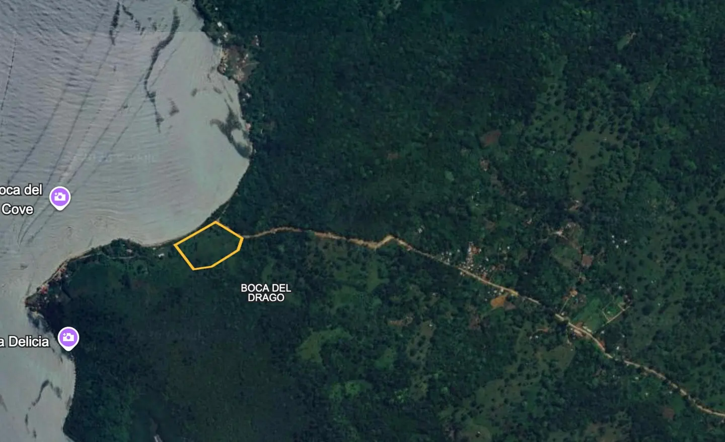 Aerial view of Boca Del Drago, Panama, showing a green lot outlined in yellow, next to the ocean and lush forest.
