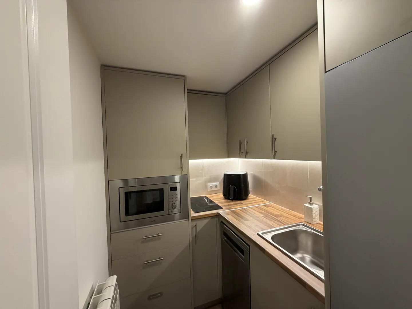 A compact kitchen with gray cabinets, stainless steel microwave, wood countertops, and a sink.