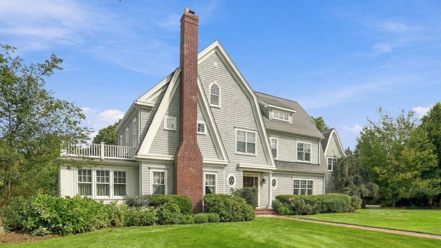 Two-story gray shingle house with a prominent red brick chimney, white trim, and a manicured lawn under a blue sky. [AI-generated text]