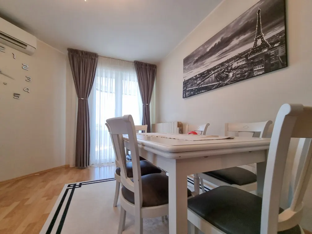 A bright dining room with a white table and chairs, a black and white Eiffel Tower print, and gray curtains.