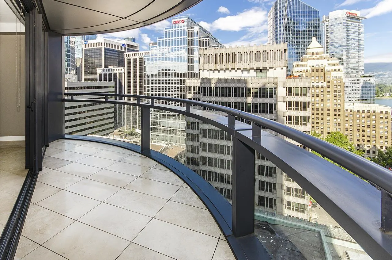 View from a curved balcony with gray railings, overlooking a cityscape with tall buildings under a blue sky.