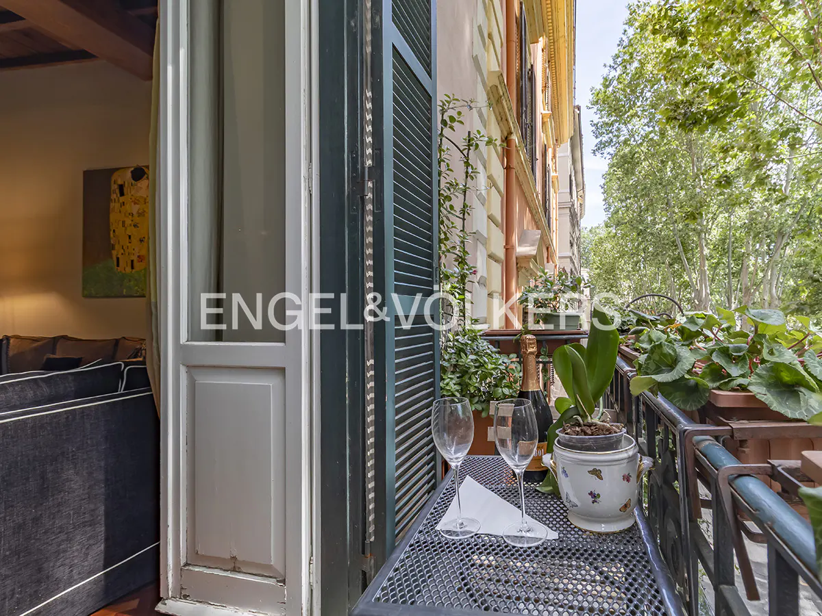 Balcony view with champagne, glasses, and plants. Open door to living room with Klimt painting. Engel & Völkers logo visible.