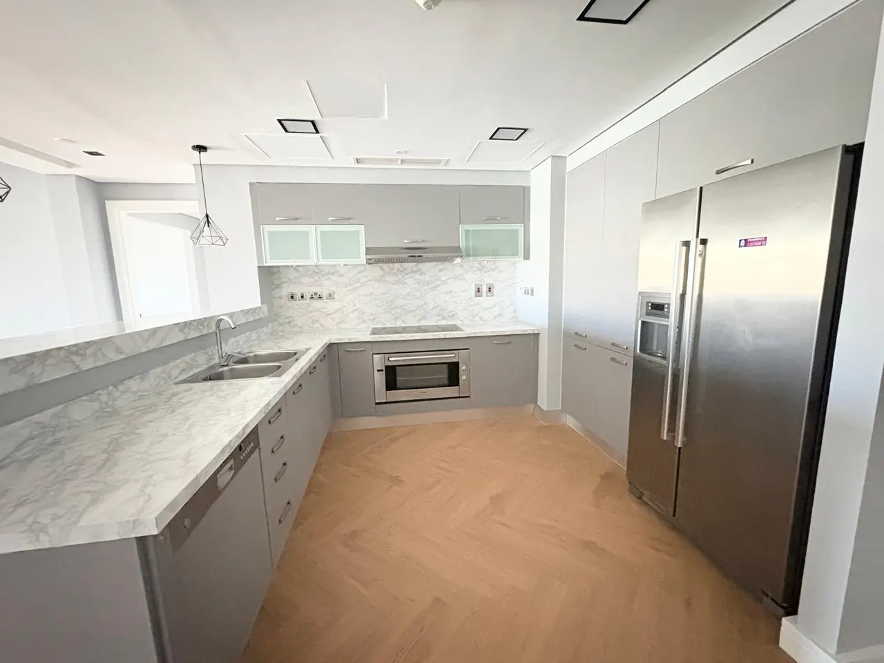 A modern kitchen with gray cabinets, marble countertops, and stainless steel appliances. The floor is light brown wood.