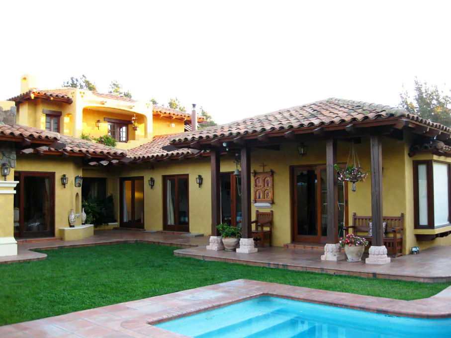 Exterior view of a yellow stucco house with a red tile roof, a green lawn, and a blue swimming pool.