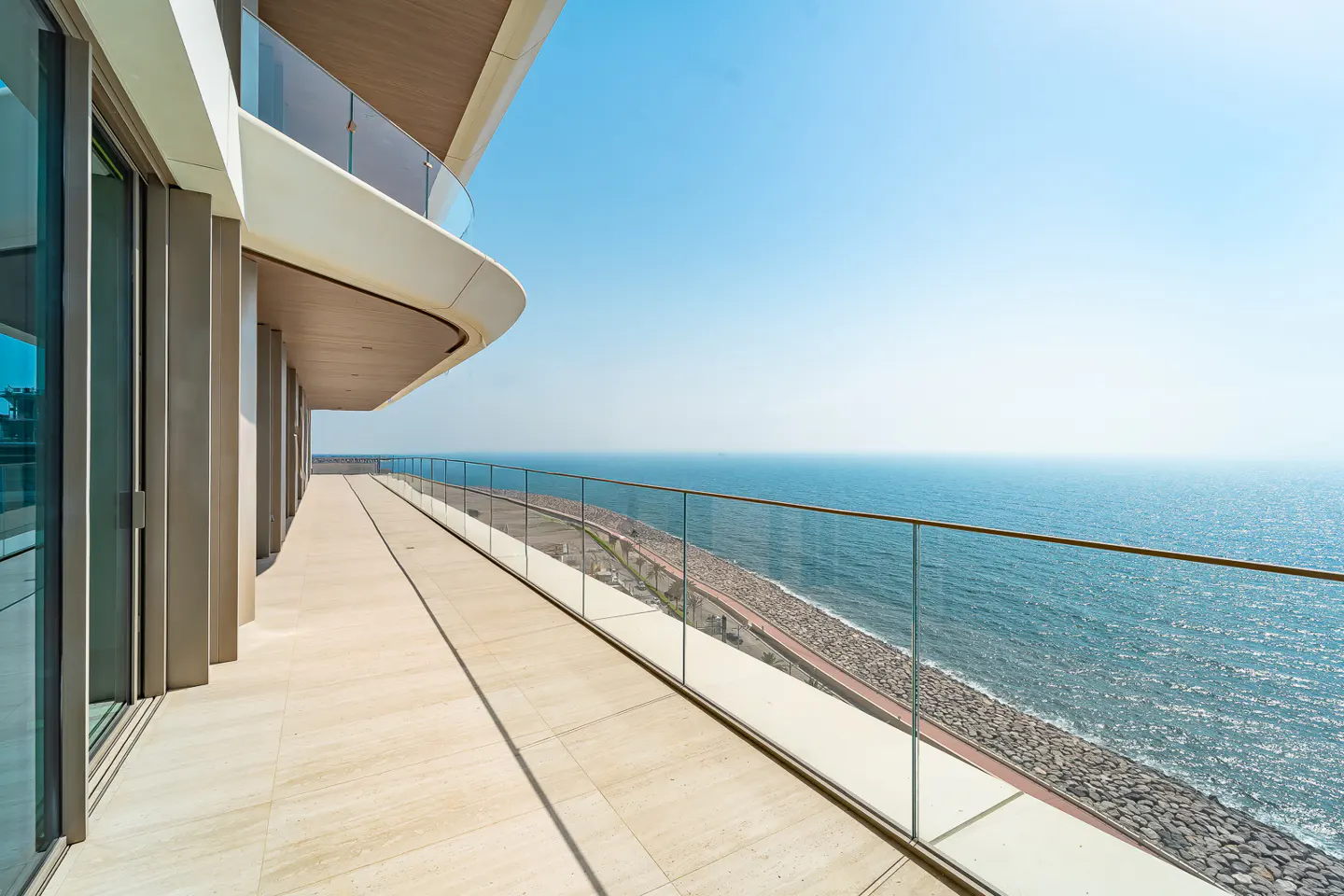 A modern balcony with glass railings overlooks the ocean on a sunny day.