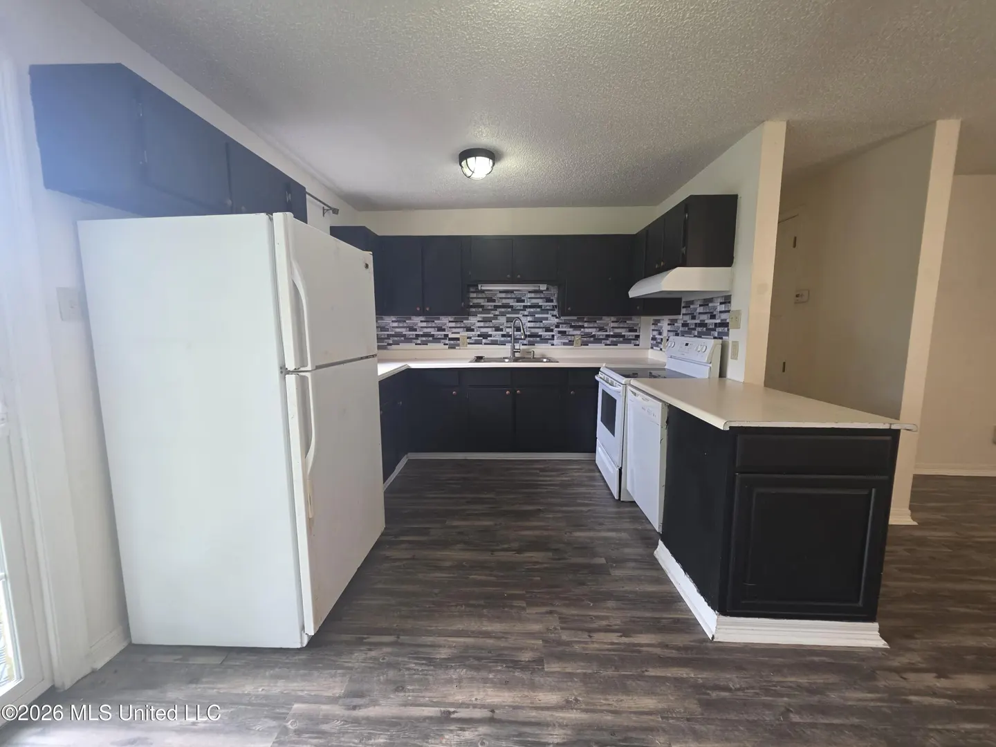 Kitchen with dark cabinets, white appliances, a patterned tile backsplash, and wood-look flooring.