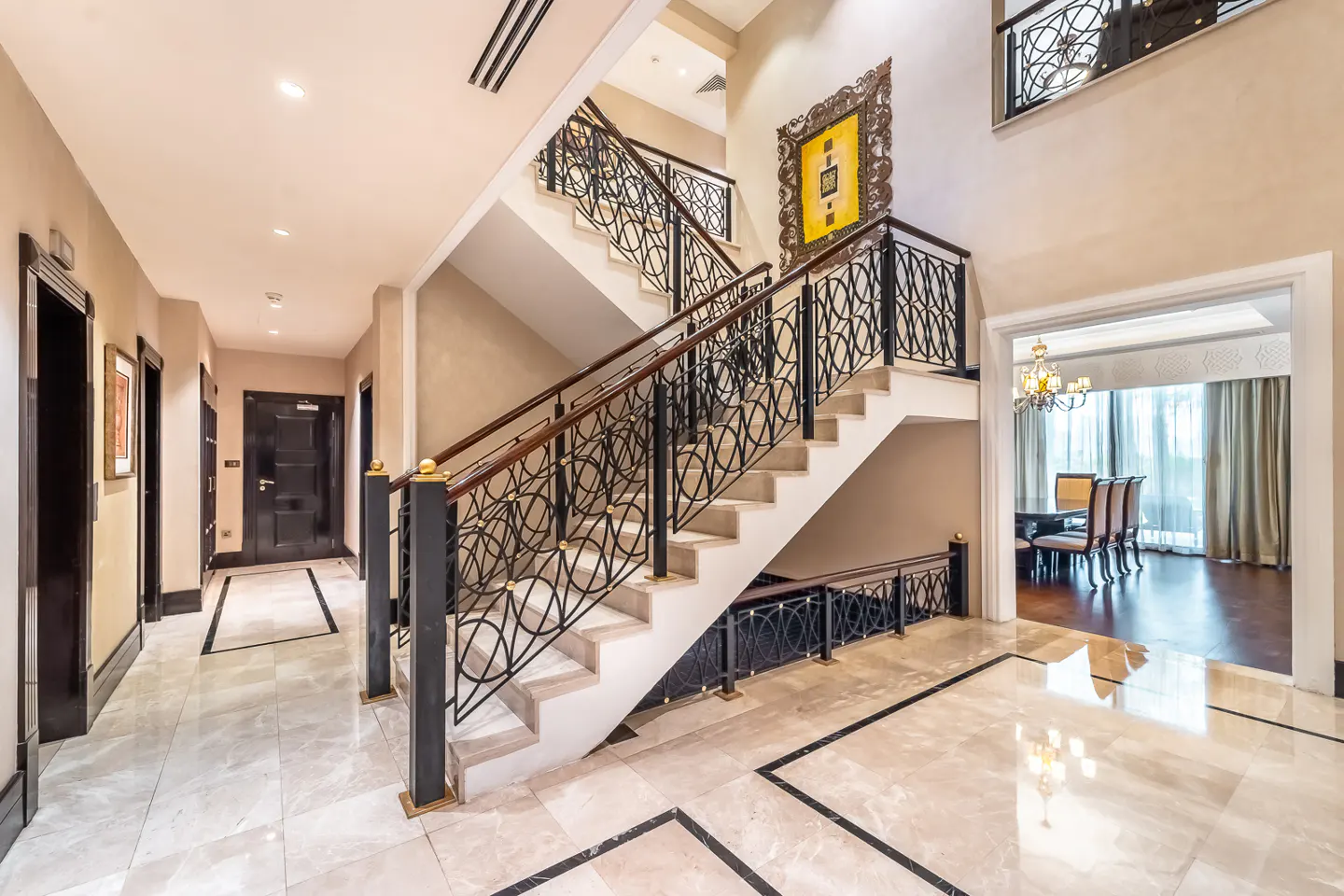 Elegant foyer with marble floors, a staircase with black wrought iron railings, and a dining room visible through an archway.