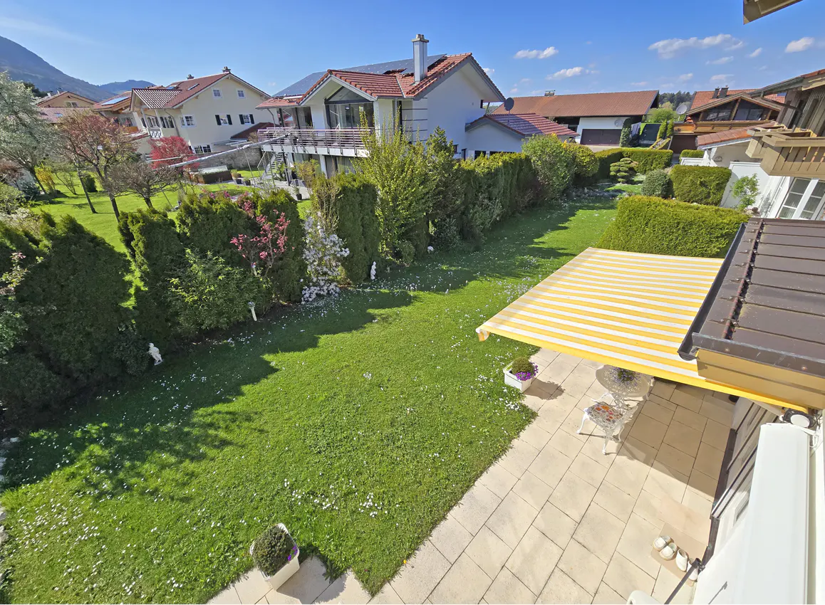 A high angle view of a green lawn with a yellow and white striped awning over a patio. Houses are in the background.