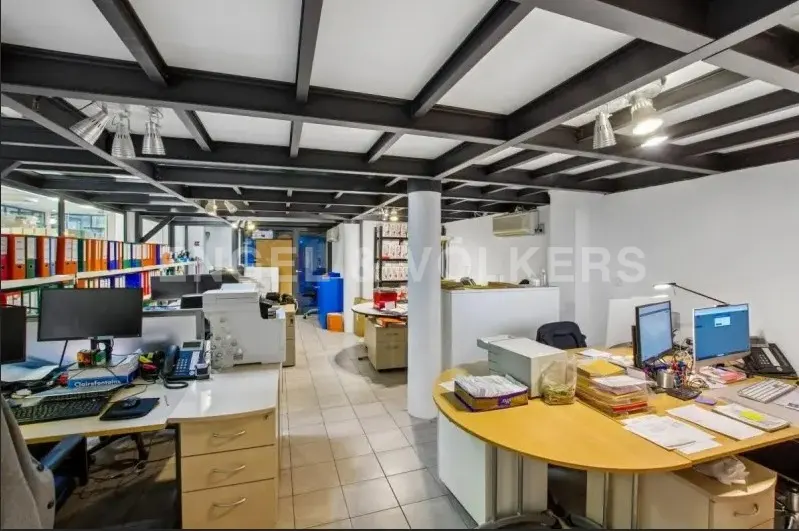 Open office space with desks, computers, and filing cabinets. Black ceiling beams and white walls create a modern look.