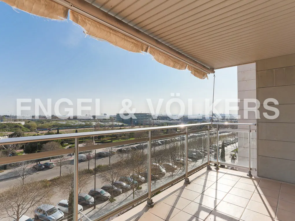 Covered balcony with tiled floor, glass railing, and a view of a street with parked cars and distant buildings.