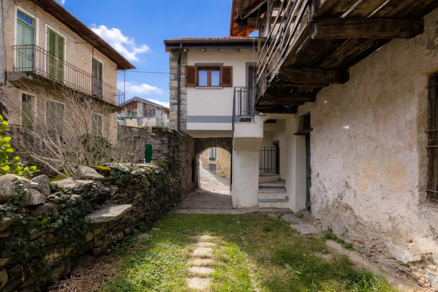 Exterior view of a stone alleyway between buildings, leading to an archway and a cobblestone street.