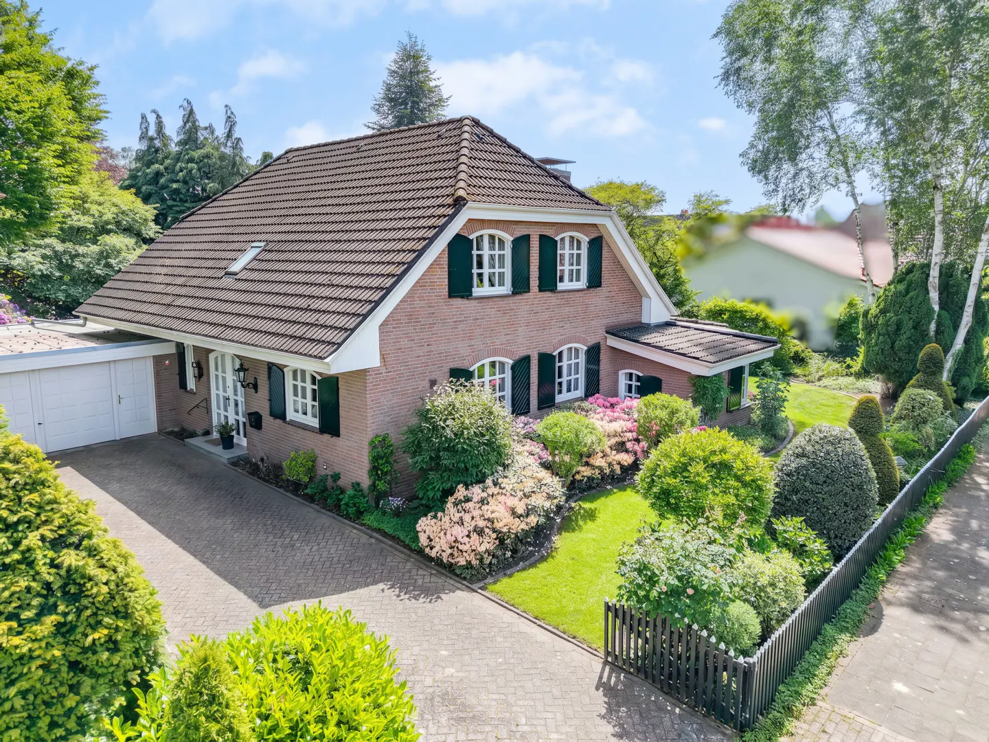 Aerial view of a brick house with a brown roof, green shutters, and a well-manicured garden.