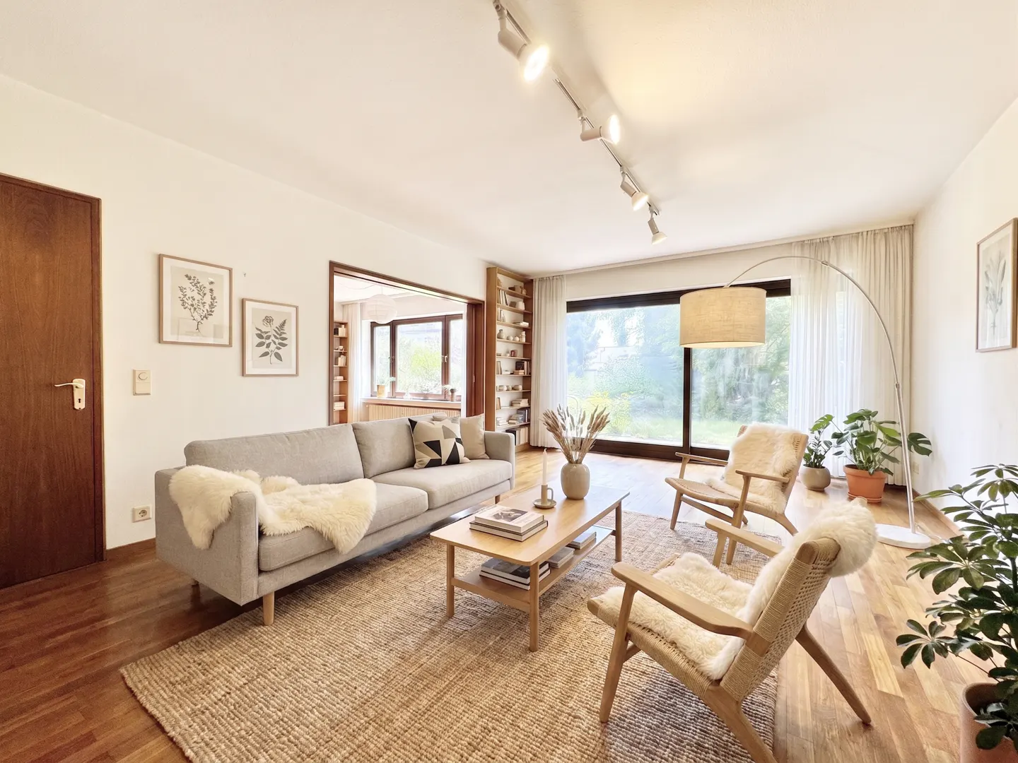 Bright living room with a gray sofa, wood chairs, and a jute rug. A large window overlooks a green yard.