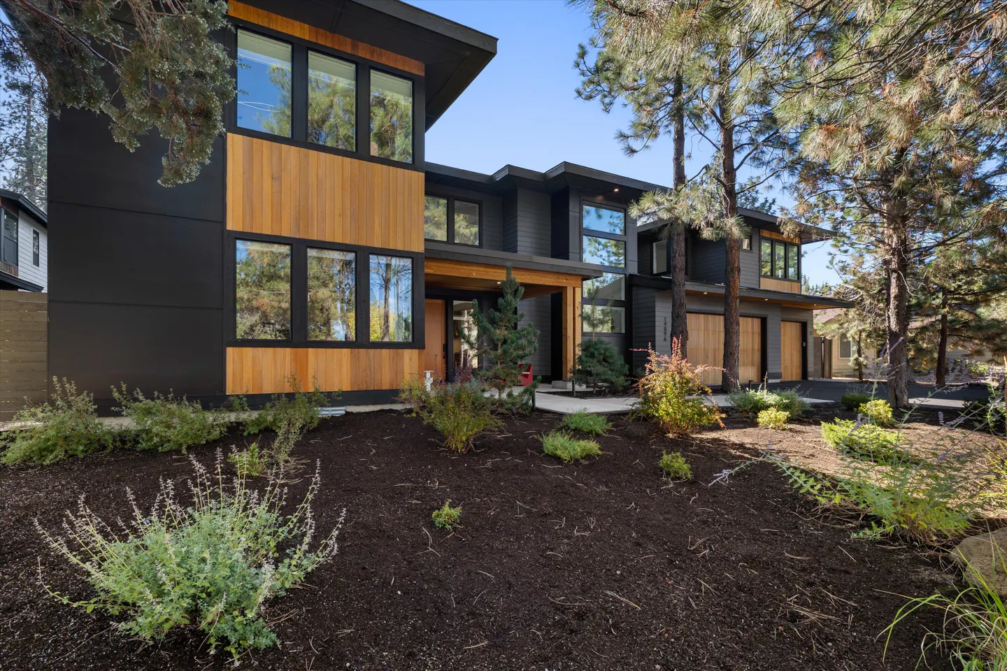Modern two-story home with black and wood siding, large windows, and landscaped yard with trees.