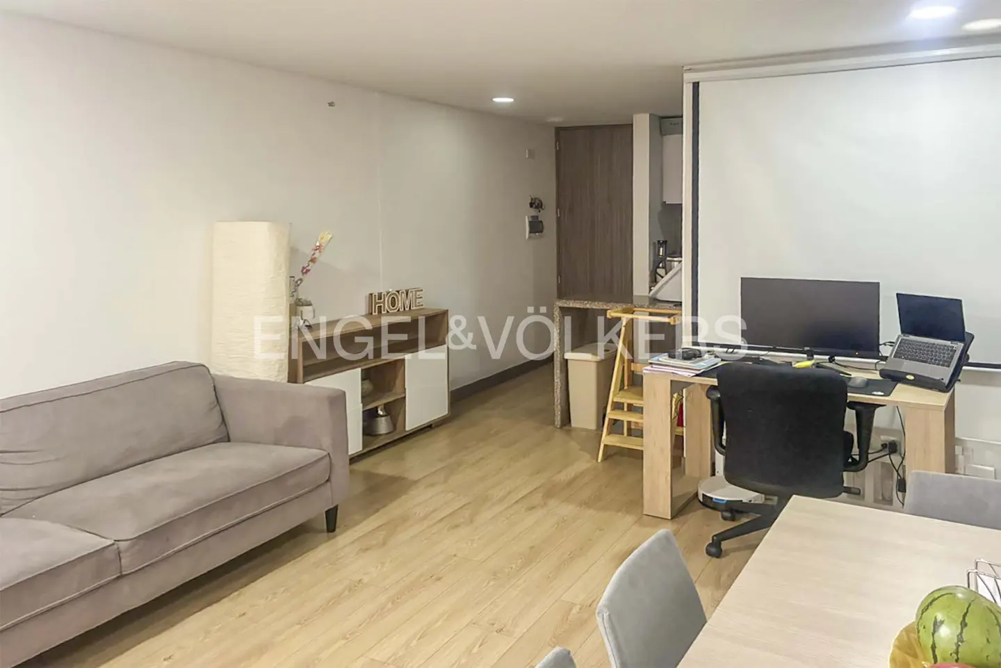 Living room with a gray sofa, wooden floors, a desk with a computer, and a white projector screen.