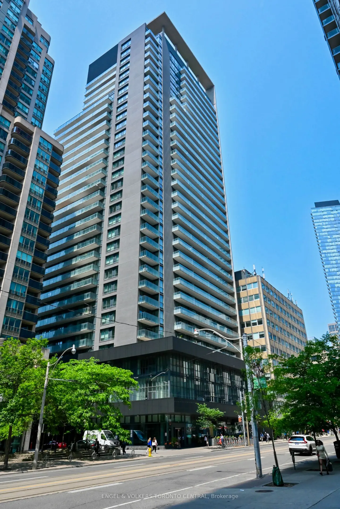Modern high-rise condo building with glass balconies, set against a clear blue sky in a bustling urban environment.
