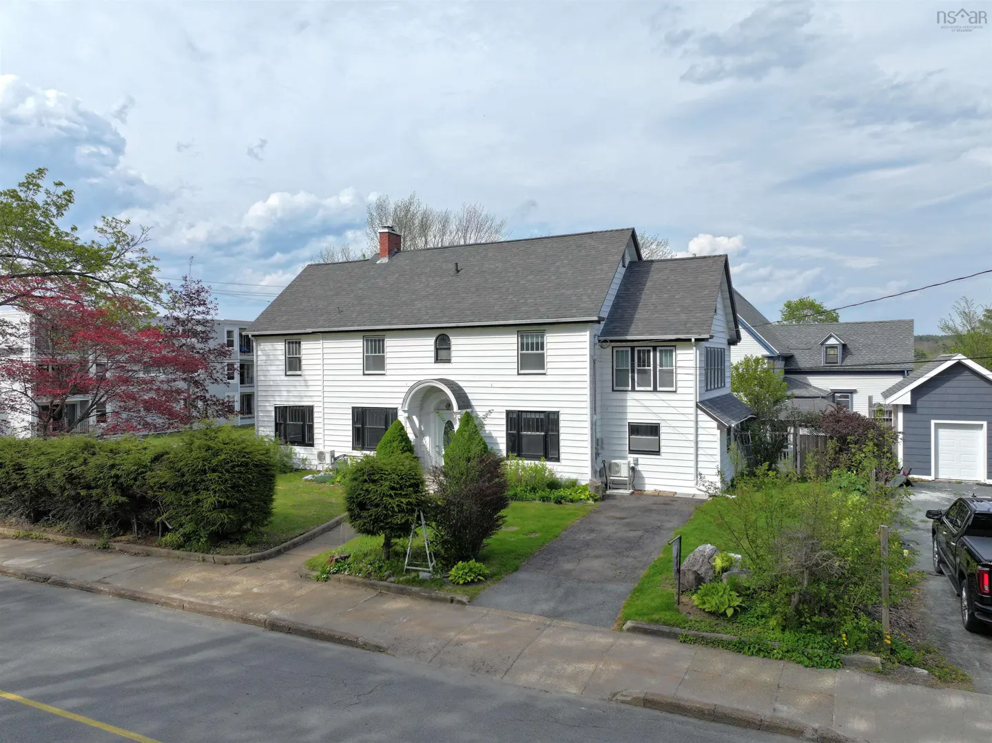 Two-story white house with a gray roof, black shutters, and a curved archway over the front door. A black truck is parked in the driveway.