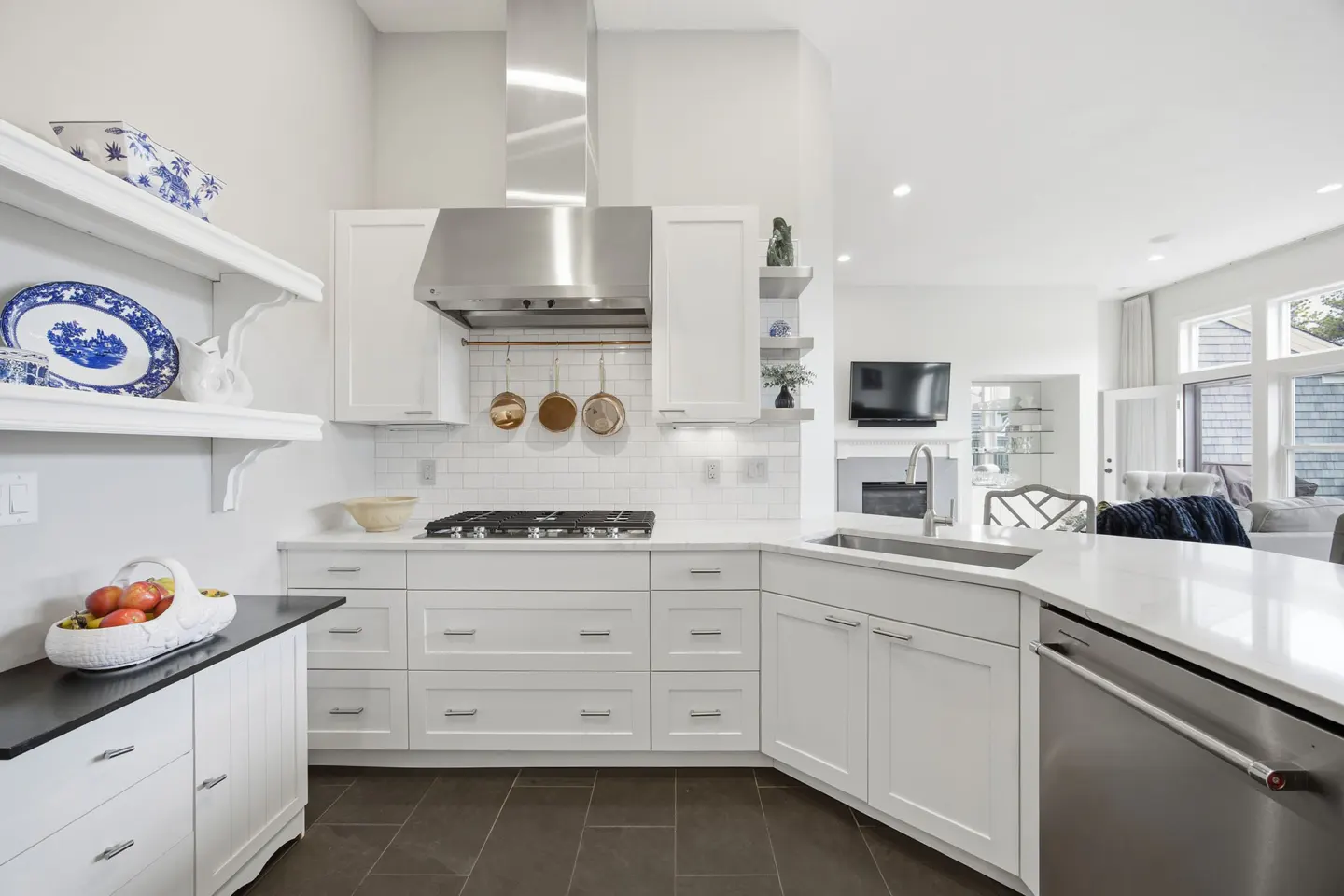 Bright, modern kitchen with white cabinets, stainless steel appliances, and dark tile floors. Open shelving displays decorative plates.