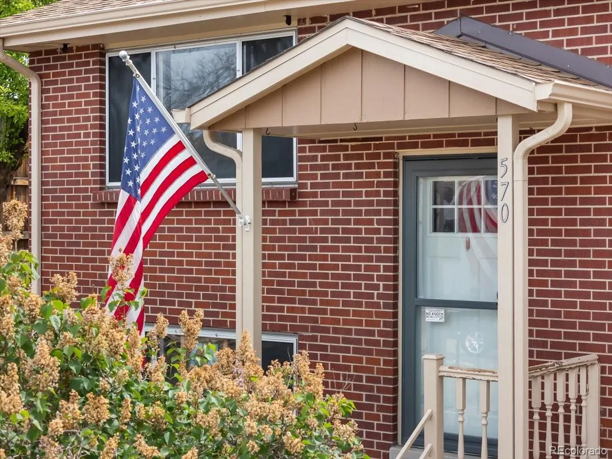 Exterior of a red brick house with an American flag waving in front of a window. The house number "570" is on a porch column.